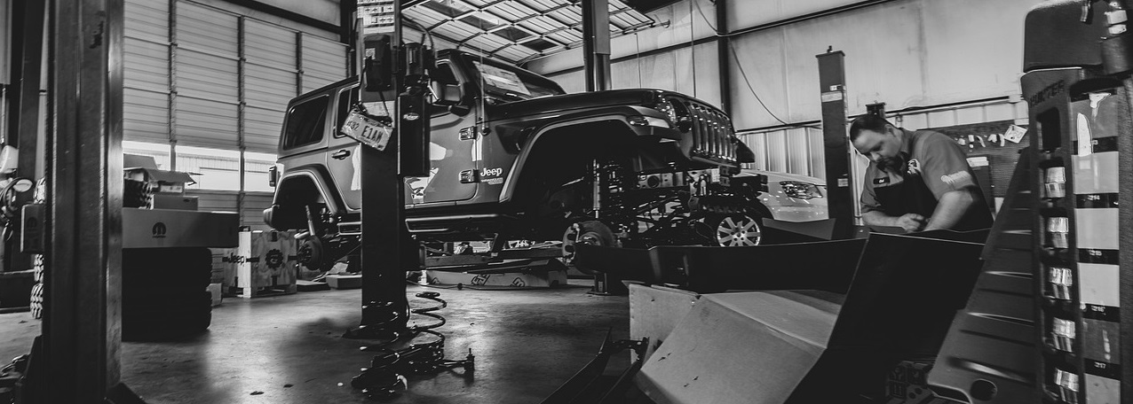 A jeep is lifted in an automotive shop where a mechanic is working